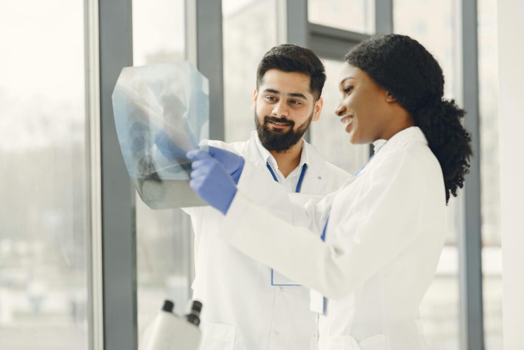 Two doctors in lab coats examine an X-ray image in a bright medical facility.